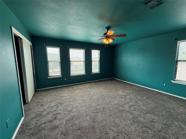 carpeted empty room with a textured ceiling, plenty of natural light, and visible vents