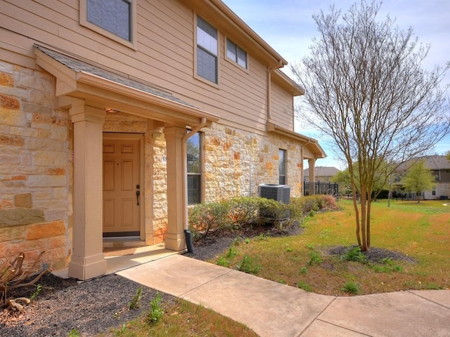 property entrance featuring a yard, central AC, and stone siding