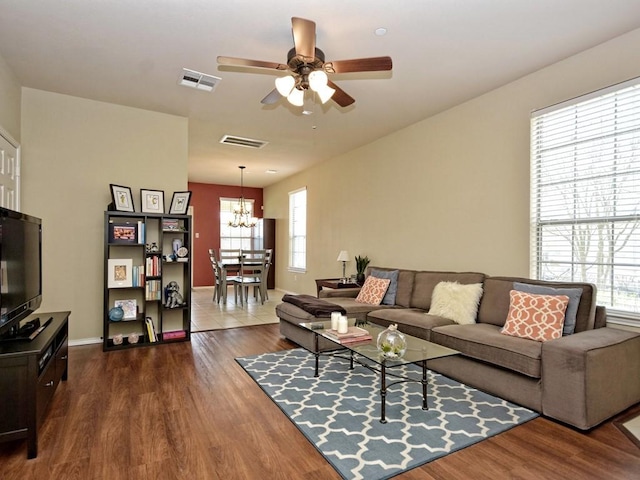 living area featuring a wealth of natural light, visible vents, and ceiling fan with notable chandelier