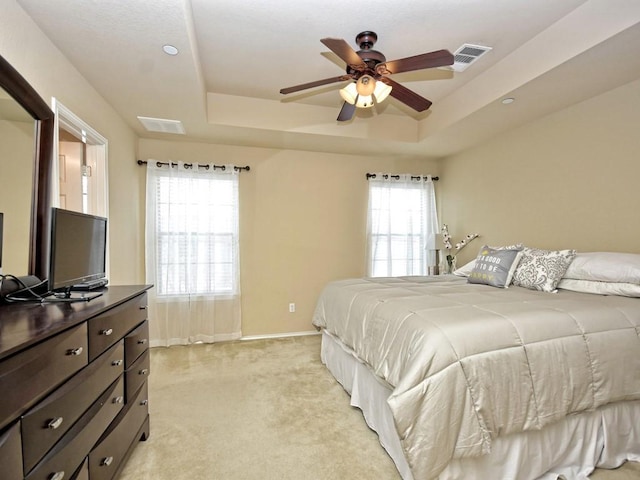 bedroom featuring light carpet, visible vents, a raised ceiling, and multiple windows