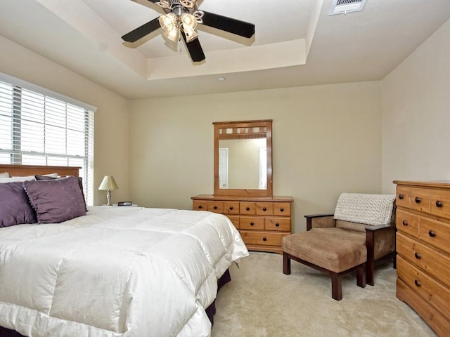 bedroom with light colored carpet, ceiling fan, visible vents, and a raised ceiling