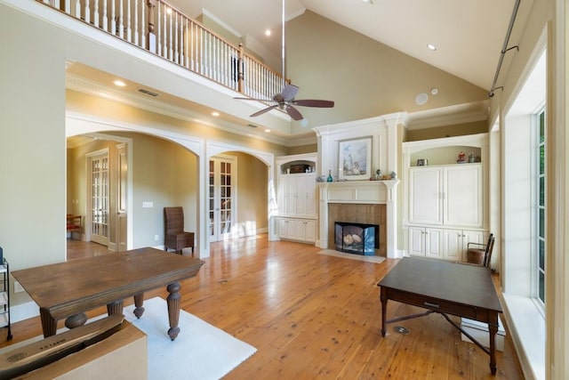 living area with a tile fireplace, visible vents, a ceiling fan, arched walkways, and high vaulted ceiling