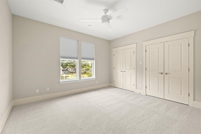 unfurnished bedroom with multiple closets, baseboards, light colored carpet, and a ceiling fan