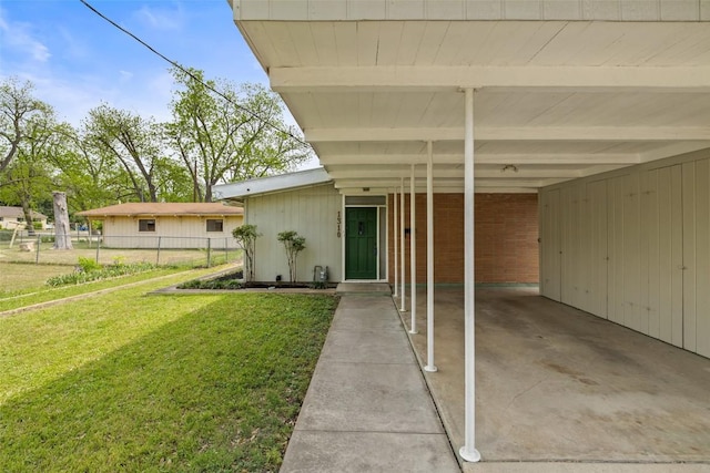 view of exterior entry featuring a yard, fence, and an attached carport