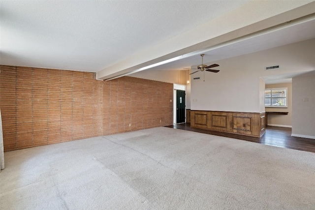unfurnished living room featuring carpet, visible vents, beam ceiling, brick wall, and ceiling fan