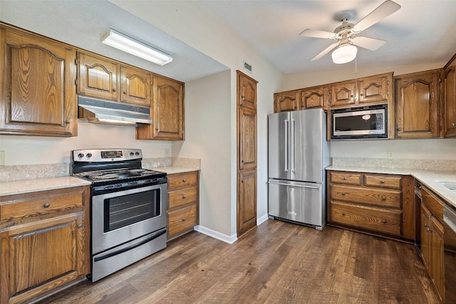 1310 Thompson St, Taylor, TX 76574 - kitchen featuring appliances with stainless steel finishes, under cabinet range hood, dark wood-type flooring, ceiling fan, and brown cabinetry