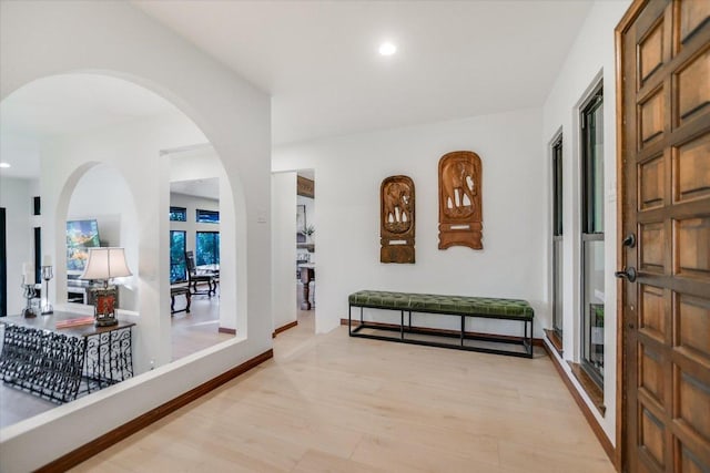 hallway featuring arched walkways, baseboards, recessed lighting, and light wood-style floors