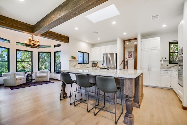 kitchen with a sink, light wood-style floors, stainless steel appliances, light stone countertops, and visible vents