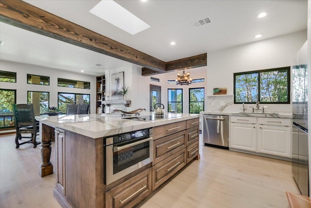 kitchen featuring recessed lighting, light stone counters, stainless steel appliances, a sink, and white cabinetry