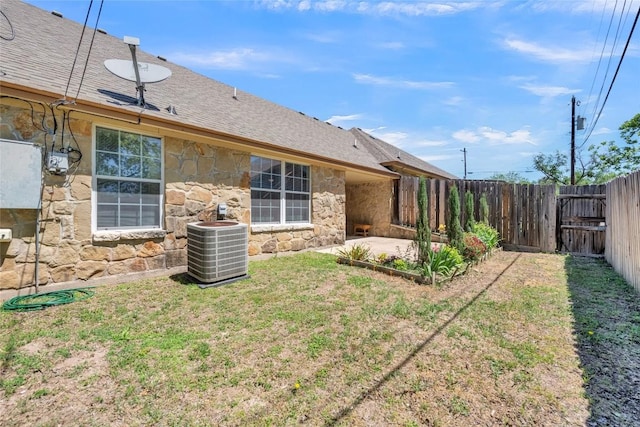 exterior space with fence, stone siding, cooling unit, roof with shingles, and a patio area