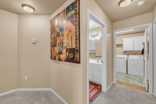 corridor featuring carpet floors, a sink, baseboards, and washing machine and dryer