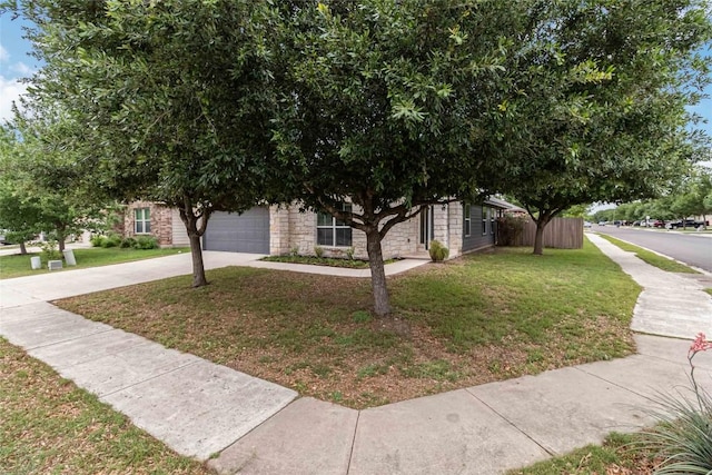view of property hidden behind natural elements with fence, concrete driveway, an attached garage, stone siding, and a front yard