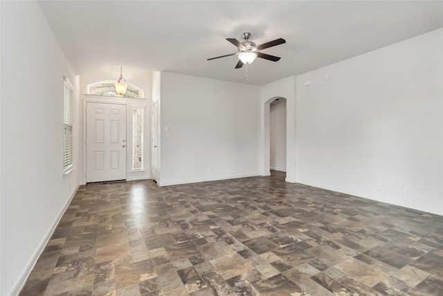 unfurnished living room with ceiling fan, arched walkways, and baseboards