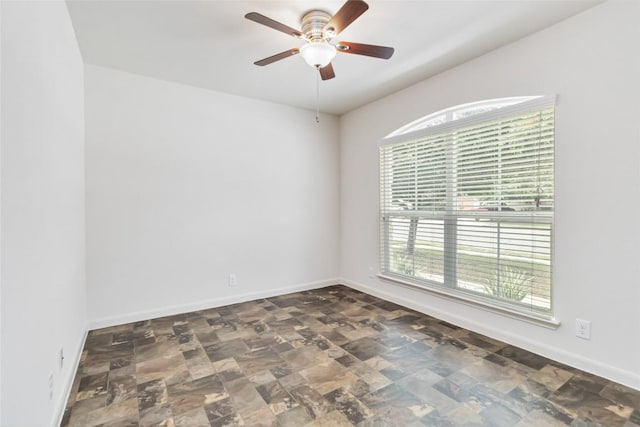 unfurnished room with ceiling fan, baseboards, a healthy amount of sunlight, and stone finish floor