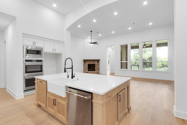 394 Leaning Rock Rdg, Austin, TX 78737 - kitchen with a ceiling fan, a sink, appliances with stainless steel finishes, a brick fireplace, and light wood-type flooring
