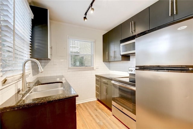 kitchen with dark stone countertops, a sink, stainless steel appliances, light wood finished floors, and rail lighting
