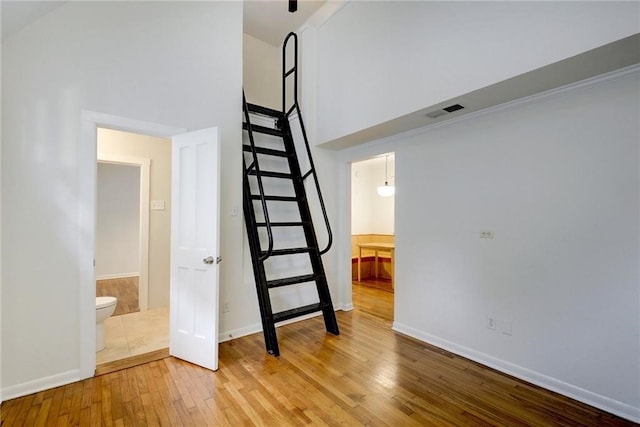 interior space with a towering ceiling, wood finished floors, visible vents, and baseboards