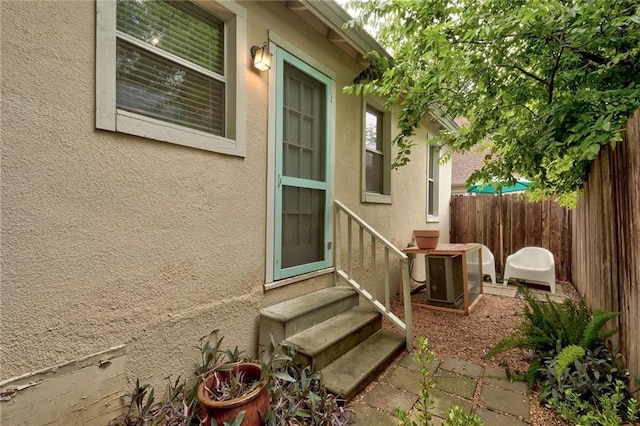 property entrance with central air condition unit, stucco siding, and fence