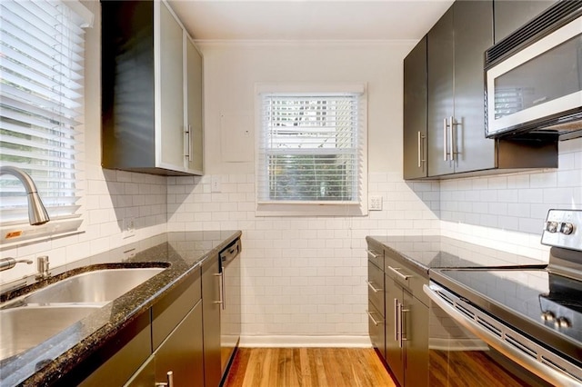 kitchen with stainless steel appliances, dark stone countertops, ornamental molding, a sink, and light wood-type flooring