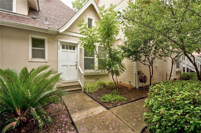 entrance to property featuring roof with shingles and stucco siding