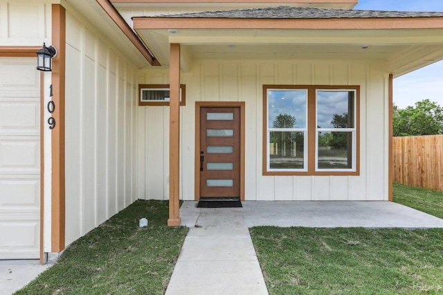 property entrance featuring fence, board and batten siding, and a yard