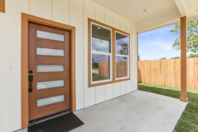 view of exterior entry featuring board and batten siding, a patio area, and fence