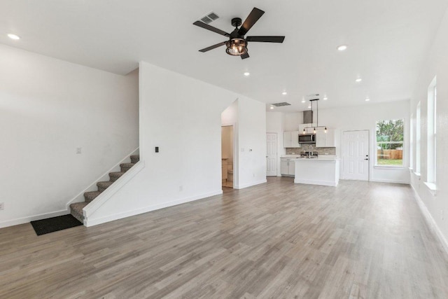 unfurnished living room featuring light wood-style flooring, visible vents, stairs, and ceiling fan