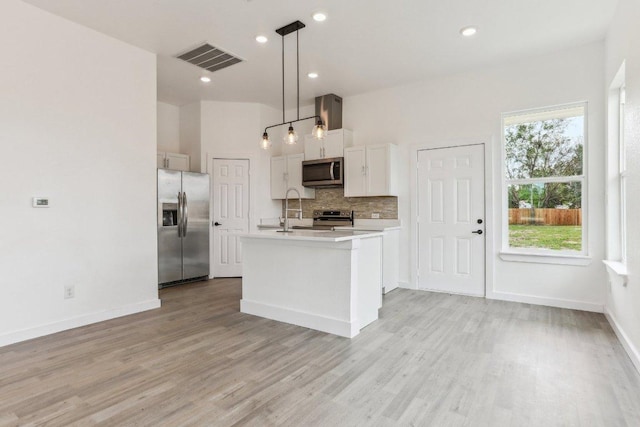 kitchen featuring stainless steel appliances, light countertops, visible vents, light wood-style floors, and tasteful backsplash
