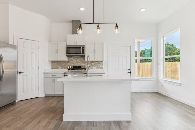kitchen with wood finished floors, a sink, decorative backsplash, light countertops, and appliances with stainless steel finishes