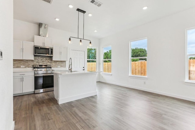 kitchen featuring stainless steel appliances, light countertops, wood finished floors, visible vents, and decorative backsplash