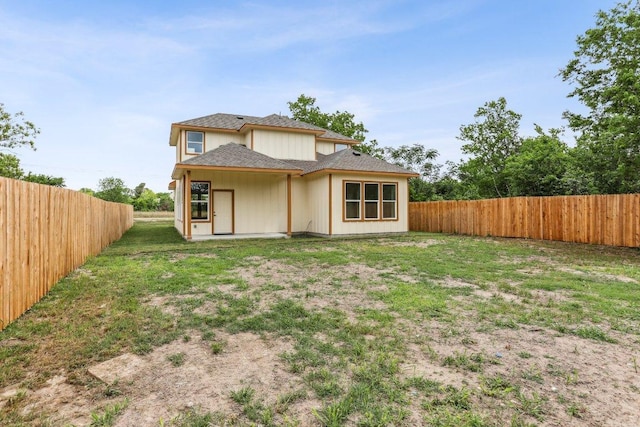 rear view of property featuring a fenced backyard, roof with shingles, and a yard