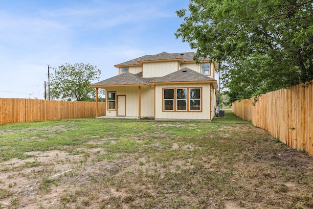 back of property with a fenced backyard, a yard, and a shingled roof