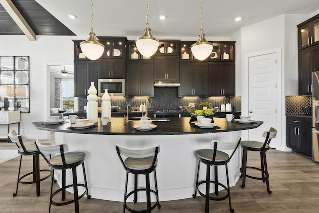 2104 Tobiano Trce, Georgetown, TX 78633 - kitchen featuring stainless steel microwave, dark countertops, decorative backsplash, a spacious island, and dark wood-style flooring