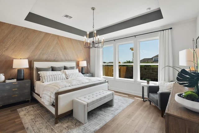 2104 Tobiano Trce, Georgetown, TX 78633 - bedroom with a raised ceiling, wooden walls, a chandelier, wood finished floors, and baseboards