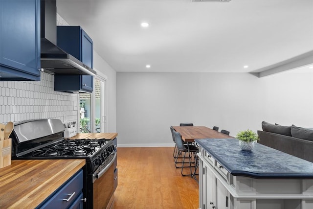 3400 Santa Fe Dr, Austin, TX 78741 - kitchen featuring stainless steel range with gas stovetop, wall chimney exhaust hood, blue cabinetry, butcher block counters, and light wood-style floors