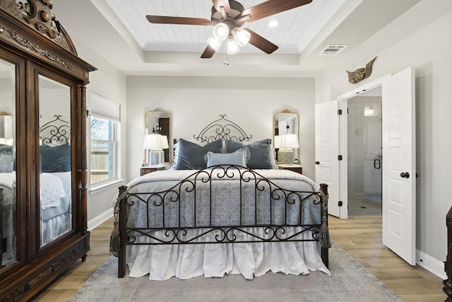 bedroom featuring ornamental molding, a tray ceiling, visible vents, and light wood-style flooring