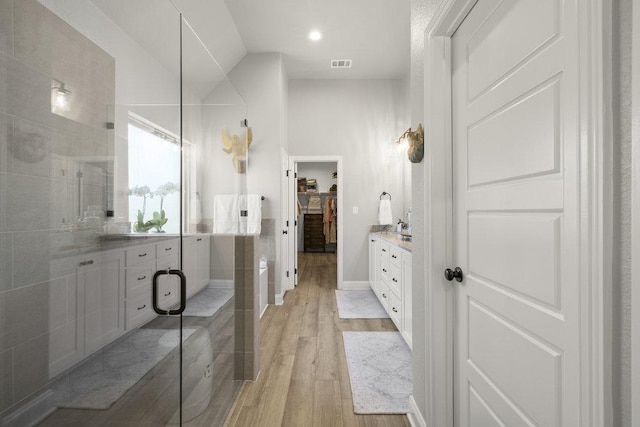 full bath with wood finished floors, visible vents, vanity, a walk in closet, and baseboards