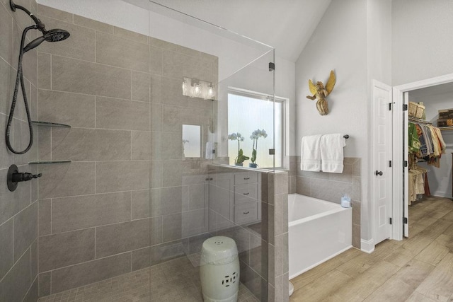bathroom with vaulted ceiling, a garden tub, wood finished floors, a walk in closet, and a tile shower