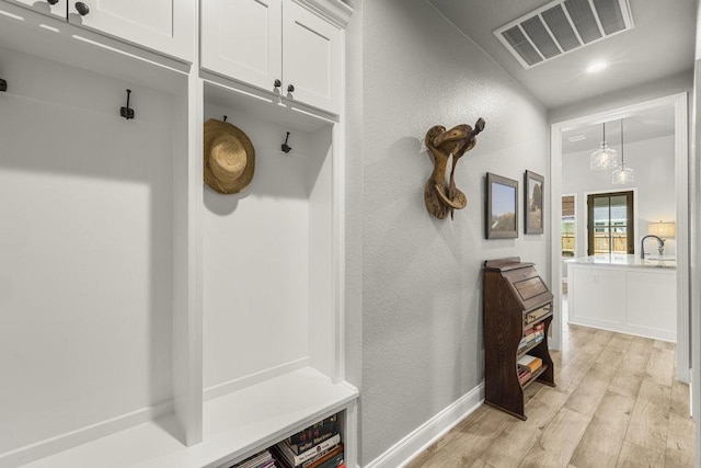 mudroom with a sink, light wood-style floors, a textured wall, baseboards, and visible vents