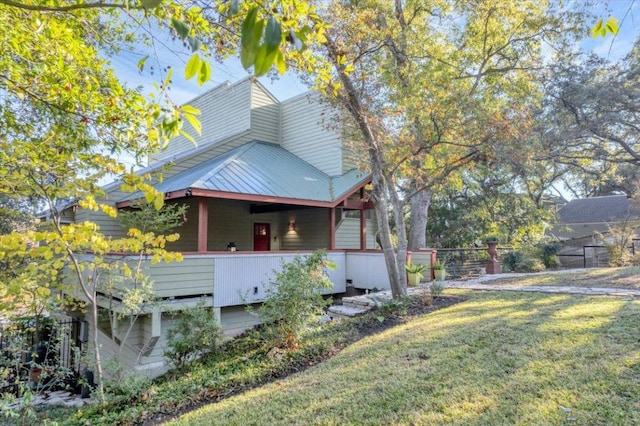 view of home's exterior with a lawn, fence, metal roof, and covered porch