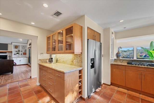 8509 Appalachian Dr, Austin, TX 78759 - kitchen with stainless steel fridge with ice dispenser, decorative backsplash, brown cabinetry, glass insert cabinets, and light stone countertops