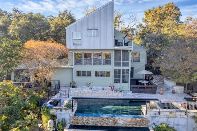 back of house featuring a swimming pool, stairs, a balcony, a sunroom, and a patio