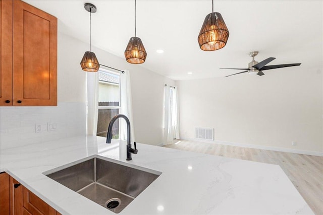 6007 Wideleaf Dr, Austin, TX 78724 - kitchen with brown cabinets, a sink, light wood-type flooring, light stone countertops, and decorative light fixtures