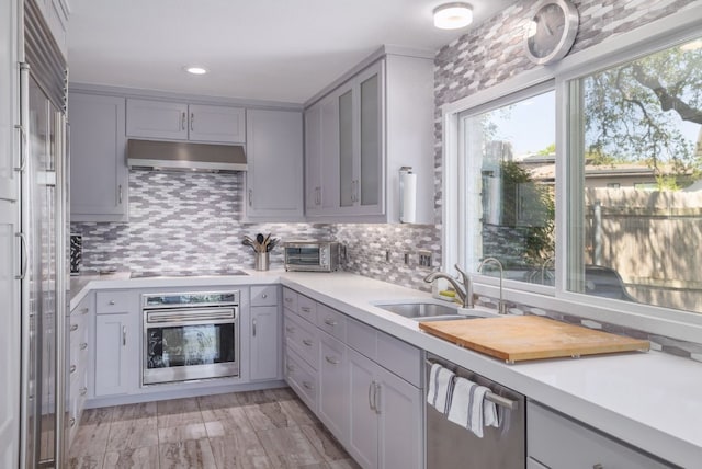 kitchen featuring under cabinet range hood, stainless steel appliances, light countertops, gray cabinets, and a sink