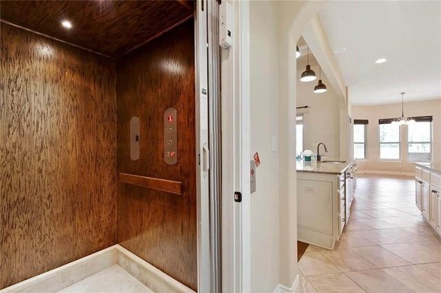hall featuring a sink, arched walkways, elevator, a chandelier, and light tile patterned floors