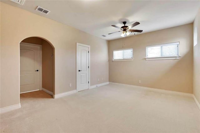 unfurnished room featuring ceiling fan, visible vents, arched walkways, baseboards, and light carpet