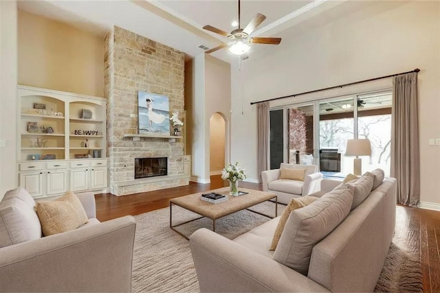 living room featuring a high ceiling, a fireplace, a ceiling fan, and wood finished floors