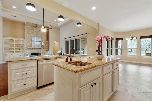 kitchen with stainless steel dishwasher, light stone countertops, open floor plan, a center island with sink, and a sink