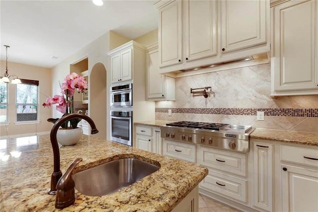 kitchen with backsplash, pendant lighting, a sink, light stone counters, and stainless steel appliances
