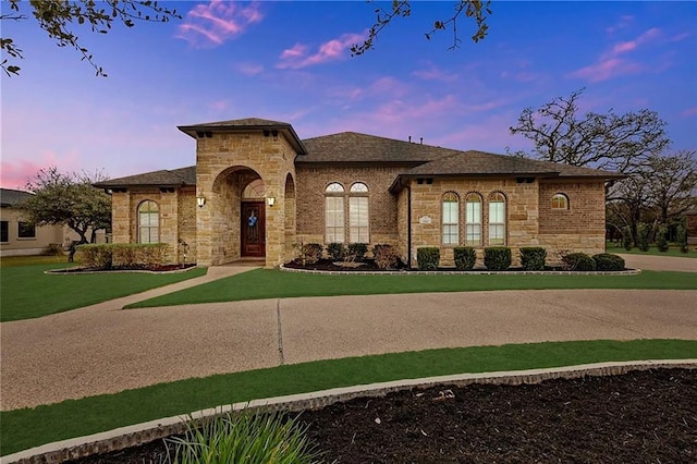 mediterranean / spanish home featuring a front yard, a shingled roof, and stone siding
